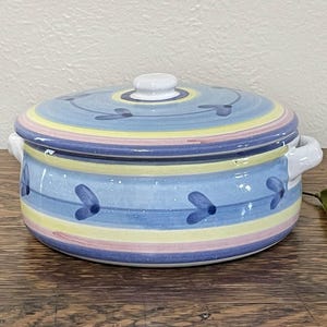 May include: A blue and yellow ceramic casserole dish with a lid. The dish has a floral design with blue flowers and green leaves. The lid has a white knob.