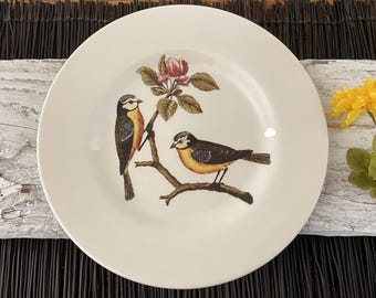 May include: White ceramic plate with a floral design featuring two birds and a pink flower. The birds are perched on a branch with green leaves.