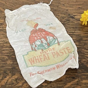 May include: Vintage white cloth bag with a printed design. The bag features the text "Pure Wheat Paste" and "Cover the Earth" in red, yellow, and green. The bag is labeled "2 LBS." and has a drawstring closure.