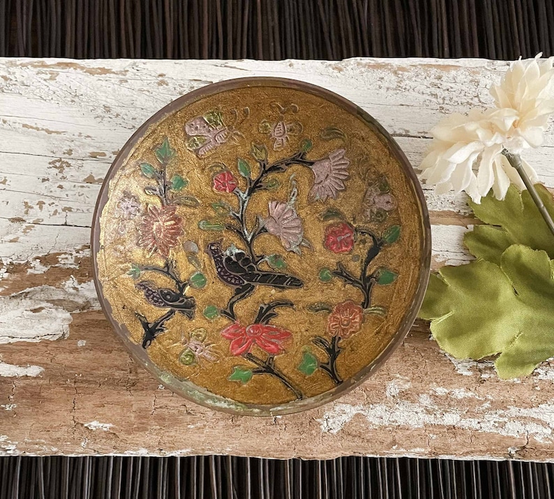 以下が含まれることがあります： 黒、赤、緑、白で描かれた複雑な花と鳥のデザインが施された、金色の仕上げの丸い真鍮のボウルです。