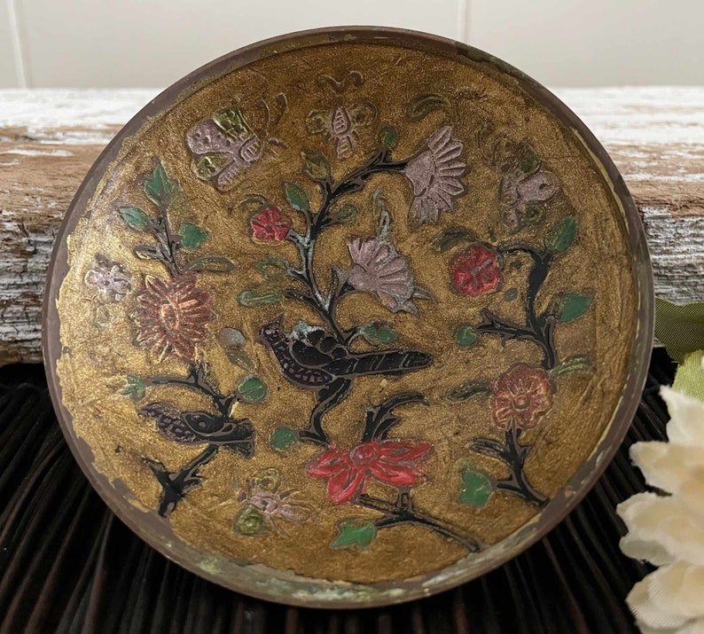 以下が含まれることがあります： 金色の背景に、黒、赤、緑、紫の花と鳥の模様が描かれた、小さな丸い真鍮製の皿です。
