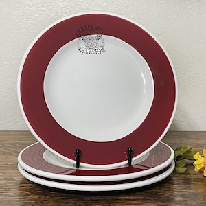 May include: Three white ceramic plates with a red rim. The top plate has the words "Dickley Mill Bakery" printed in black.