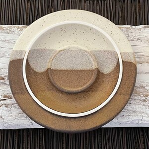 May include: A set of two ceramic plates with a speckled, layered design. The plates feature a color gradient from cream to brown, with a white rim. The smaller plate is nested inside the larger one, creating a unique serving dish.