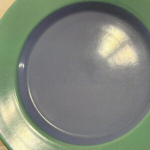 May include: A green and blue ceramic plate with a raised rim. The plate is empty and has a glossy finish.