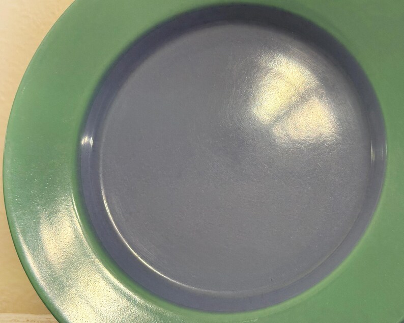 May include: A green and blue ceramic plate with a raised rim. The plate is empty and has a glossy finish.