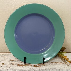 May include: A blue and green ceramic plate with a raised rim. The plate is on a white wooden surface.