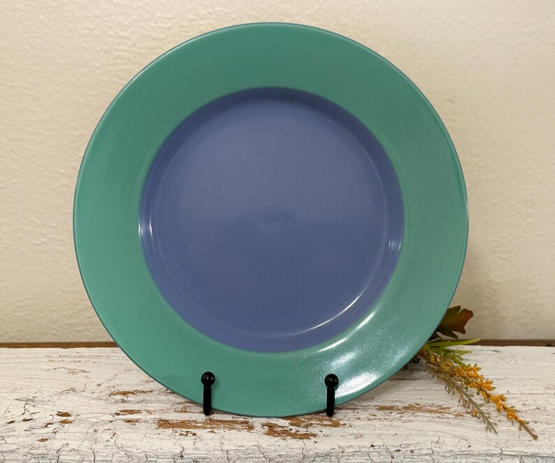 May include: A blue and green ceramic plate with a raised rim. The plate is on a white wooden surface.