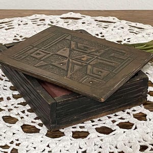 May include: A wooden box with a hinged lid. The lid is decorated with a carved geometric pattern. The box is dark brown and has a distressed finish.