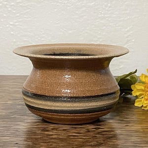 May include: A small, brown ceramic planter with a wide, flared rim and a striped design. The planter has a speckled glaze and is perfect for small plants or succulents.