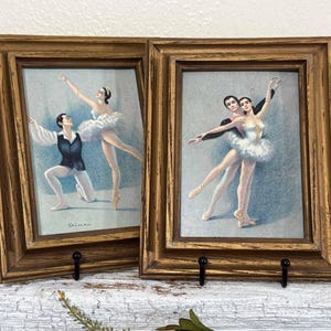May include: Two framed vintage ballet prints. Each print features a male and female dancer in a classic ballet pose. The frames are gold-toned with a distressed finish, and the prints are mounted on a light blue background.