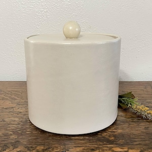 May include: A white ceramic ice bucket with a round, white lid. The lid has a small, round knob on top.