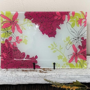 May include: A rectangular glass tray featuring a white background with a vibrant floral pattern. The design includes clusters of magenta flowers, bright lime green foliage, and delicate black line-art flower outlines across the surface.