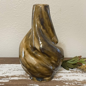 May include: A brown and white ceramic vase with a unique, swirled design. The vase has a wide base and a narrow neck.