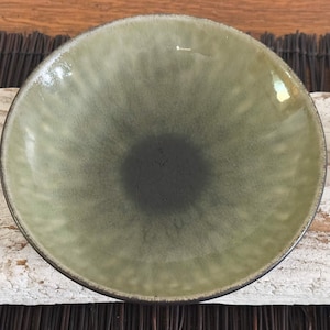 May include: A round, ceramic bowl with a gradient color scheme. The center is a dark charcoal color that fades to a light green around the edges. The rim is a dark brown color.