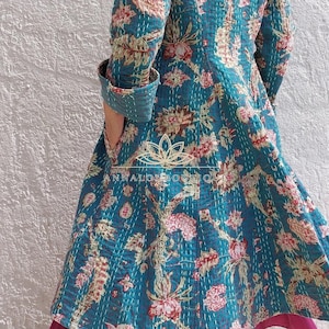 Può includere: Una giacca a maniche lunghe color verde acqua con un motivo floreale nei toni del rosa, crema e verde. Il capo presenta visibili cuciture kantha bianche su tutto il tessuto e include una tasca laterale. Il testo ANNALOUBOUTIQUE è stampato.