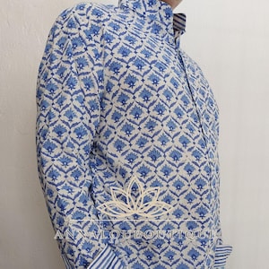 Peut inclure: Une chemise à manches longues boutonnée avec un motif floral bleu et blanc. La chemise présente un col et des poignets à rayures bleues et blanches. Le texte ANNALOUBOUTIQUE est imprimé au centre de la chemise sur le motif floral.