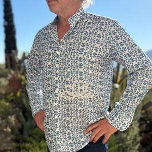 Peut inclure: Une chemise à manches longues boutonnée avec un motif floral bleu et blanc. La chemise présente un col officier et une patte de boutonnage centrale. Le texte ANNALOUBOUTIQUE est imprimé sur la partie centrale de la chemise.