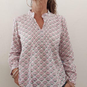 May include: A white long-sleeved blouse with a pink and green floral print. The blouse has a V-neck and a gathered detail at the neckline.