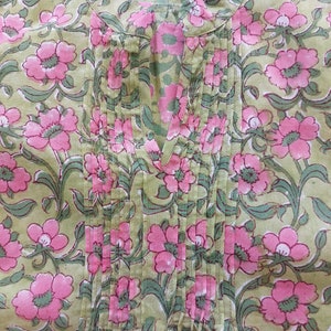 May include: A light green tunic featuring a repeating floral pattern of pink blossoms with dark green stems and leaves. The garment includes a vertical pleated panel down the center front, a notched neckline, and a mandarin-style collar detail.