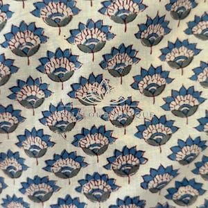 May include: A cream-colored fabric featuring a repeating pattern of blue and dark red lotus-style flowers. Centered on the textile is a white graphic logo of a lotus flower above the text ANNALOUBOUTIQUE in a clean, sans-serif font.