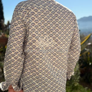 May include: A long-sleeve button-down shirt in a cream color featuring a repeating blue and orange floral pattern. The back of the shirt displays a white lotus flower graphic and the text ANNALOUBOUTIQUE printed across the center.