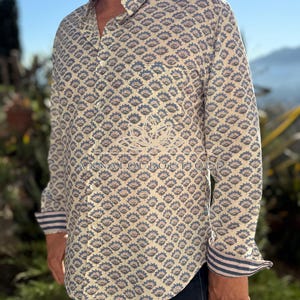 May include: A long-sleeved button-down shirt featuring a repeating blue and muted red floral block print on a cream background. The shirt includes a chest pocket, a standard collar, and cuffs with a blue and white striped pattern on the interior.