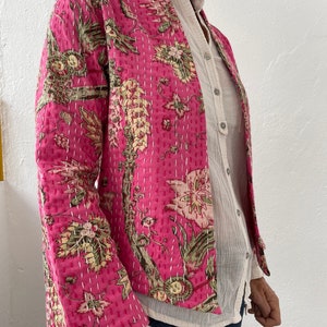 May include: A pink quilted jacket with a floral print. The jacket has a mandarin collar and a long sleeve.