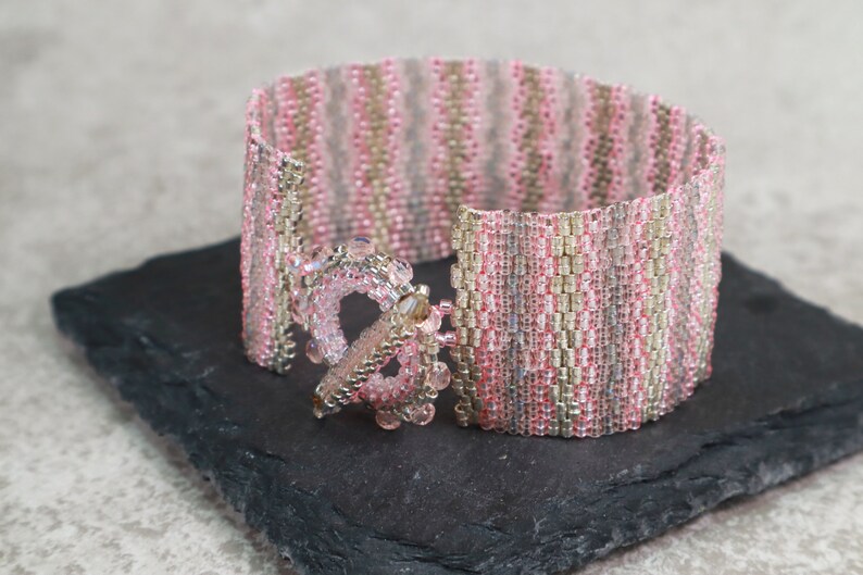 May include: A pink and silver beaded bracelet with a decorative clasp. The bracelet is made with small, seed beads and has a striped pattern.