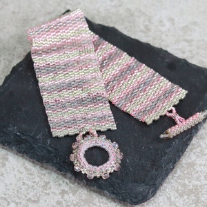 May include: A pink and silver beaded bracelet with a circular bead charm. The bracelet is made with small seed beads and has a toggle clasp.