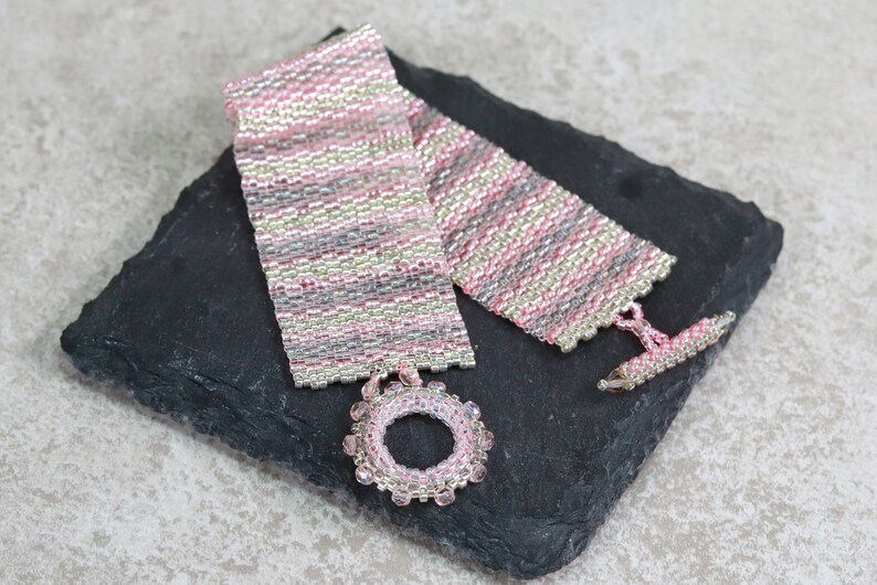 May include: A pink and silver beaded bracelet with a circular bead charm. The bracelet is made with small seed beads and has a toggle clasp.