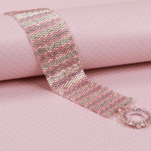 May include: A pink and silver beaded bracelet with a silver clasp. The bracelet is made with small, round beads that are arranged in a striped pattern.