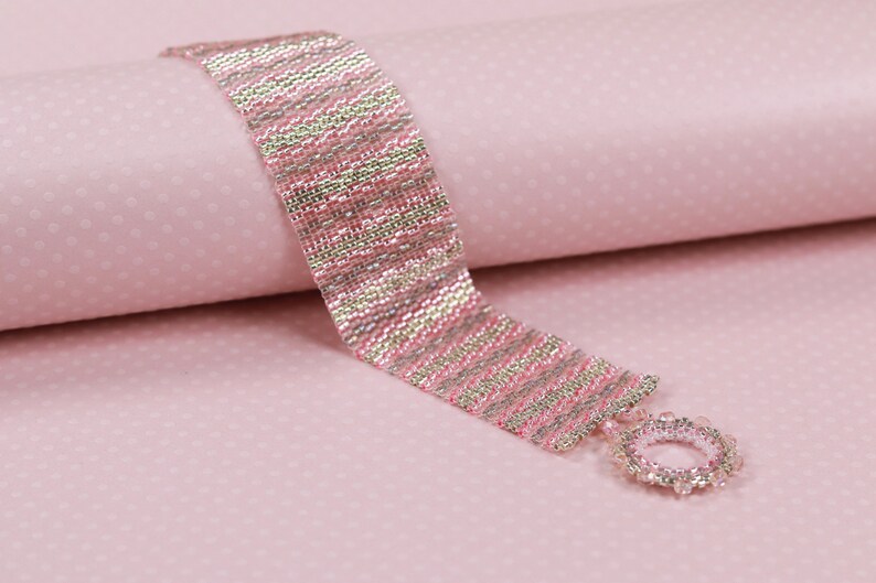 May include: A pink and silver beaded bracelet with a silver clasp. The bracelet is made with small, round beads that are arranged in a striped pattern.
