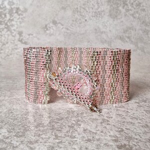 May include: A pink and silver beaded bracelet with a silver clasp. The bracelet is made of small, square beads that are arranged in a pattern.