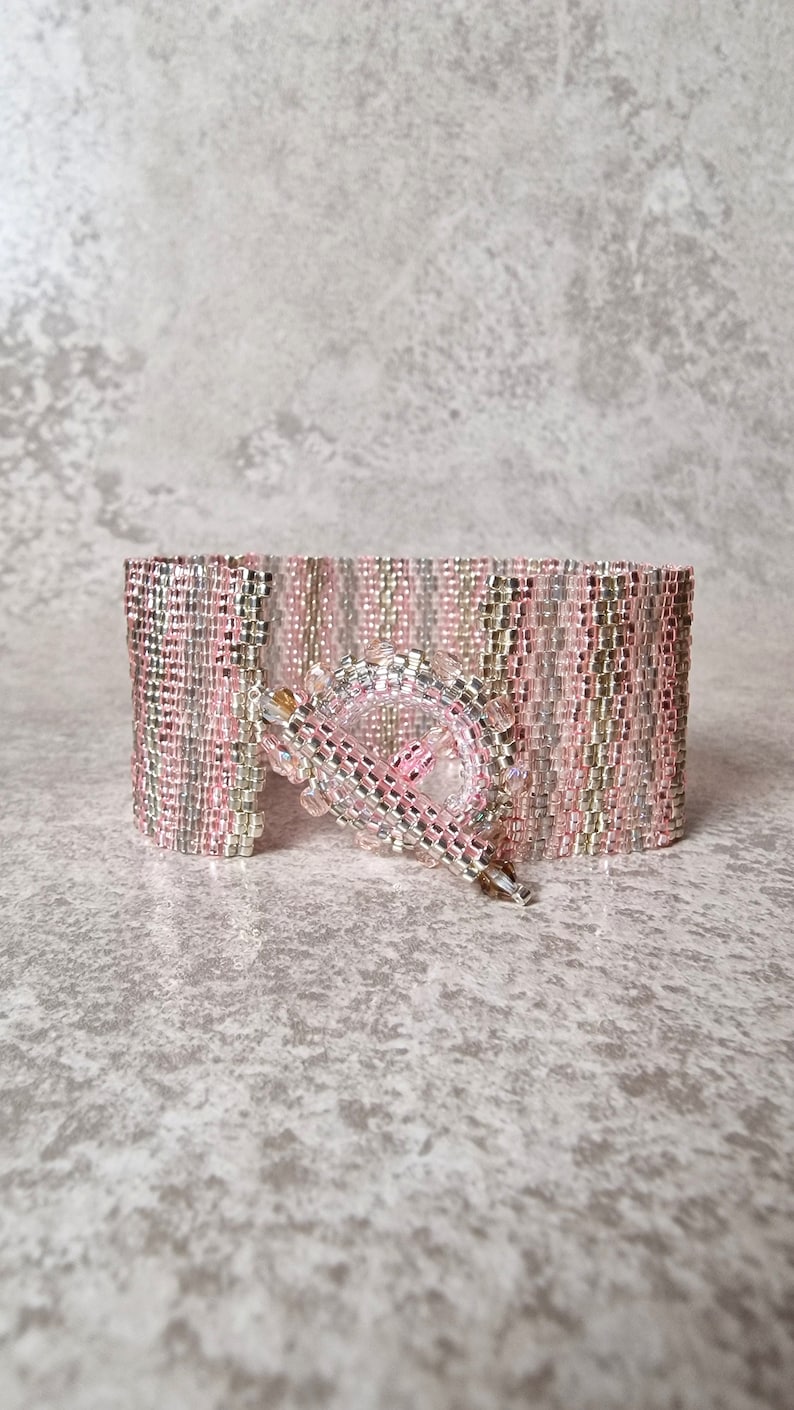 May include: A pink and silver beaded bracelet with a silver clasp. The bracelet is made of small, square beads that are arranged in a pattern.