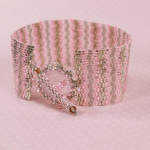 May include: A pink and silver beaded bracelet with a decorative clasp. The bracelet is made of small, square beads that are arranged in a striped pattern.