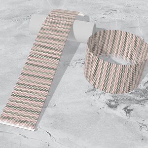 May include: A pink, green, and white patterned woven bracelet. The bracelet is shown rolled up and laid flat.