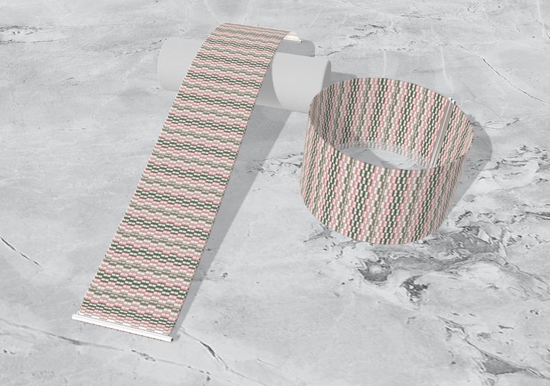 May include: A pink, green, and white patterned woven bracelet. The bracelet is shown rolled up and laid flat.