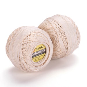 Può includere: Due gomitoli di filo color crema con un'etichetta gialla che recita "YarnArt CANARIAS www.yarnart.info 10% Cotone Mercerizzato 20g/20г 203 m/203 м"
