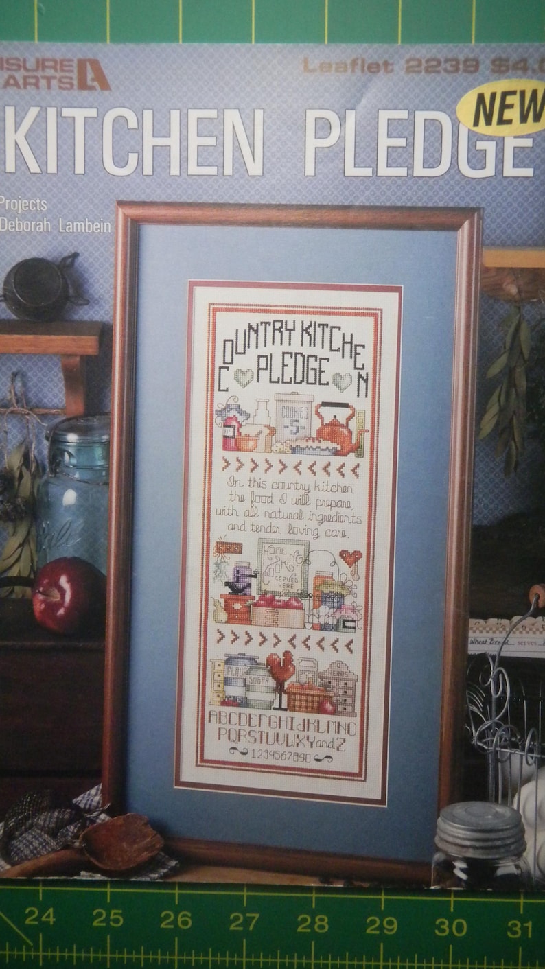 Może przedstawiać: Oprawiony haft krzyżykowy zatytułowany "Country Kitchen Pledge". Projekt zawiera motywy kuchenne, takie jak czajnik, słoiki i kogut, z tekstem: "W tej wiejskiej kuchni przygotuję jedzenie ze wszystkimi naturalnymi składnikami i delikatną, troskliwą opieką."