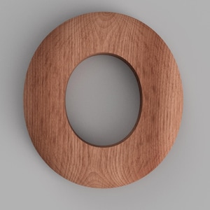 May include: A wooden letter "O" with a natural wood grain finish. The letter is a solid, circular shape with a hollow center. The wood has a warm, reddish-brown hue, and the grain is visible throughout the surface.