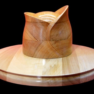 Könnte beinhalten: Ein Hut aus Holz mit breiter Krempe und einem einzigartigen, gefalteten Design. Der Hut ist aus hellbraunem Holz gefertigt und hat eine glatte, polierte Oberfläche.