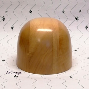 Puede incluir: Un bloque de sombrero de madera marrón claro con un acabado liso y brillante. El bloque tiene una parte superior redondeada y una base plana.