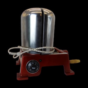 May include: A red metal base with a silver metal top and a white cord. The top has a dial with numbers and a small green light. The base has a handle on the side.
