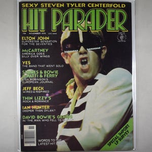 May include: A November 1976 issue of Hit Parader magazine featuring a cover image of a person wearing piano-key shaped glasses and a white jacket with black stripes. The cover text includes headlines about Elton John, McCartney, and David Bowie.