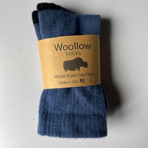 May include: A pair of blue socks with black heels and toes, wrapped in a tan paper band labeled Woollow SOCKS with a yak graphic, the text Made from Yak Fiber, and the text Made in USA with a small American flag icon.