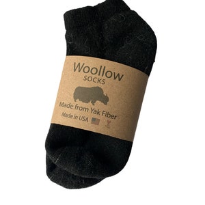 May include: A pair of black socks made from yak fiber. The socks are wrapped with a brown paper band that reads "Woollow SOCKS" with a yak silhouette, "Made from Yak Fiber" and "Made in USA".