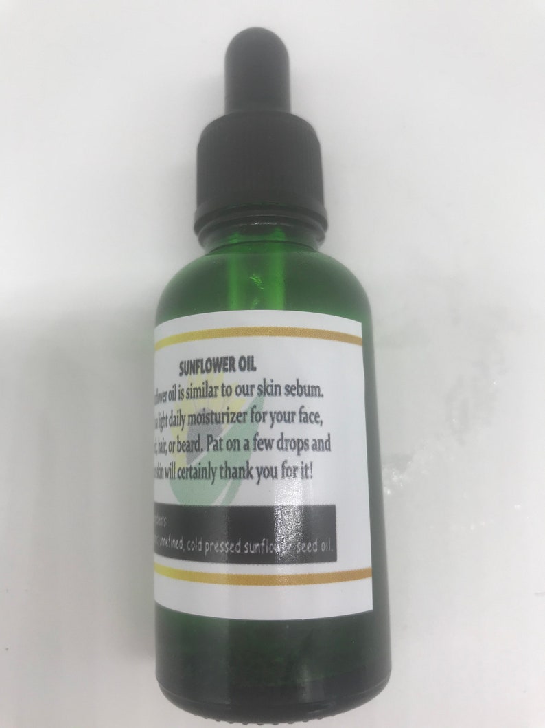 May include: A green glass bottle with a black dropper top. The label reads "SUNFLOWER OIL" and describes it as a daily moisturizer. The label also lists the ingredients as refined, cold pressed sunflower seed oil.