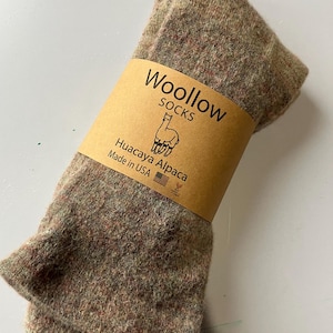 May include: A pair of brown and green alpaca wool socks folded and packaged with a brown label that reads "Woollow Socks Huacaya Alpaca Made in USA".