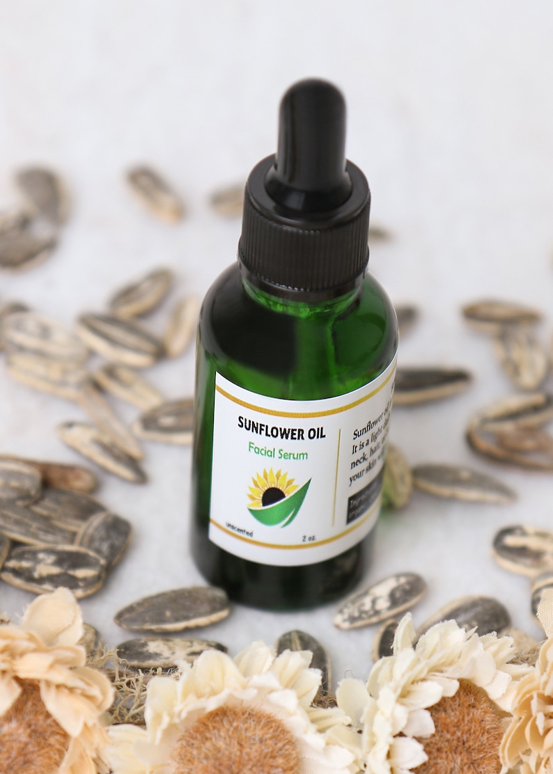 May include: A green glass bottle of Sunflower Oil Facial Serum with a black dropper. The label features a sunflower graphic and the text "Sunflower Oil Facial Serum". The bottle is surrounded by sunflower seeds and dried flowers.