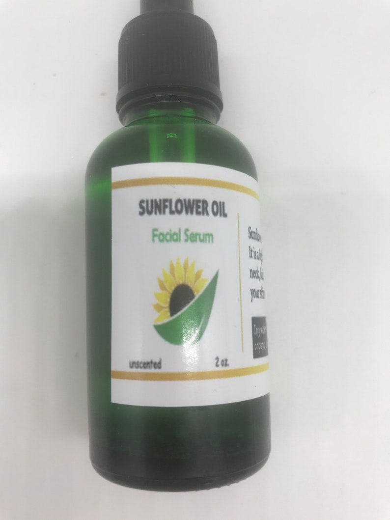 May include: A green glass bottle of Sunflower Oil Facial Serum. The label features a sunflower illustration and the text "unscented" and "2 oz.". The bottle has a black dropper top.